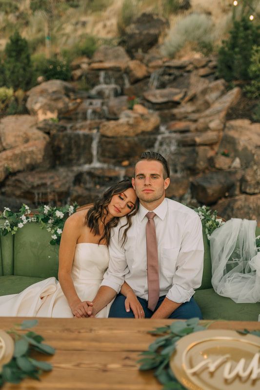 A bride and groom are sitting at a table in front of a waterfall.