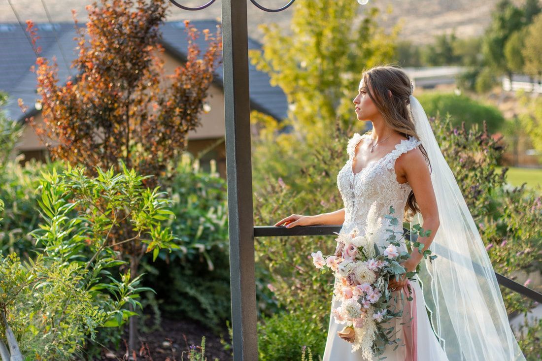 A bride in a wedding dress and veil is standing next to a railing holding a bouquet of flowers.