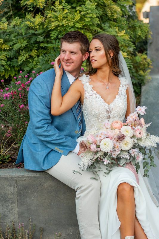 A bride and groom are sitting next to each other on a wall.