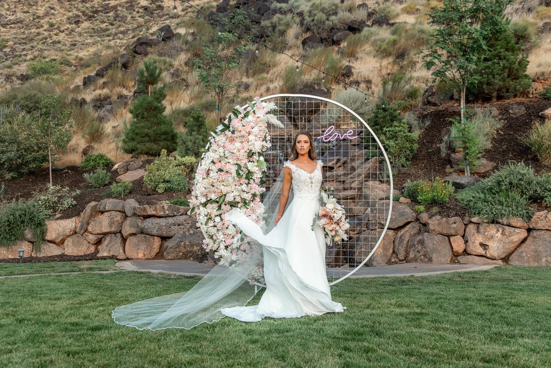 A bride in a wedding dress and veil is standing in front of a floral arch.