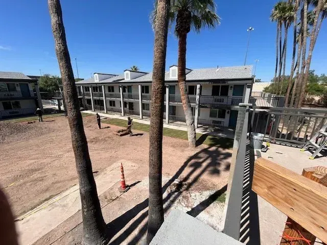 Exterior shot of a two-story motel with palm trees in the foreground. Sunny, clear day.
