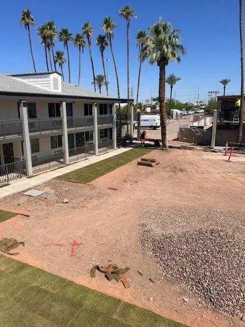 A two-story motel building next to a dirt lot with palm trees under a blue sky.