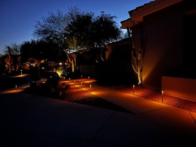 Pathway illuminated by warm lights at night, next to a house with desert landscaping.