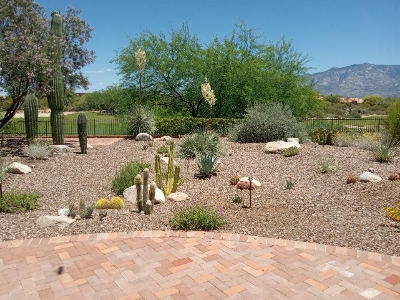 Outdoor kitchen with grill, cabinets, and granite countertops; stone columns and forest view.