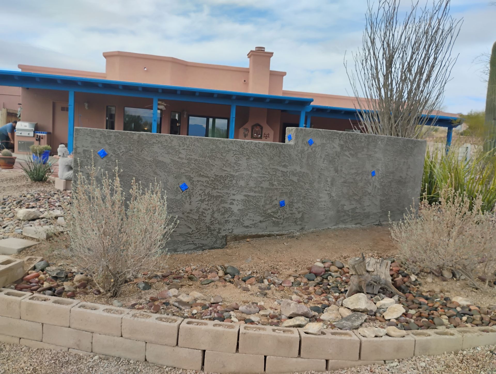 A textured concrete wall with blue tape in a desert landscape, in front of a southwest-style house.