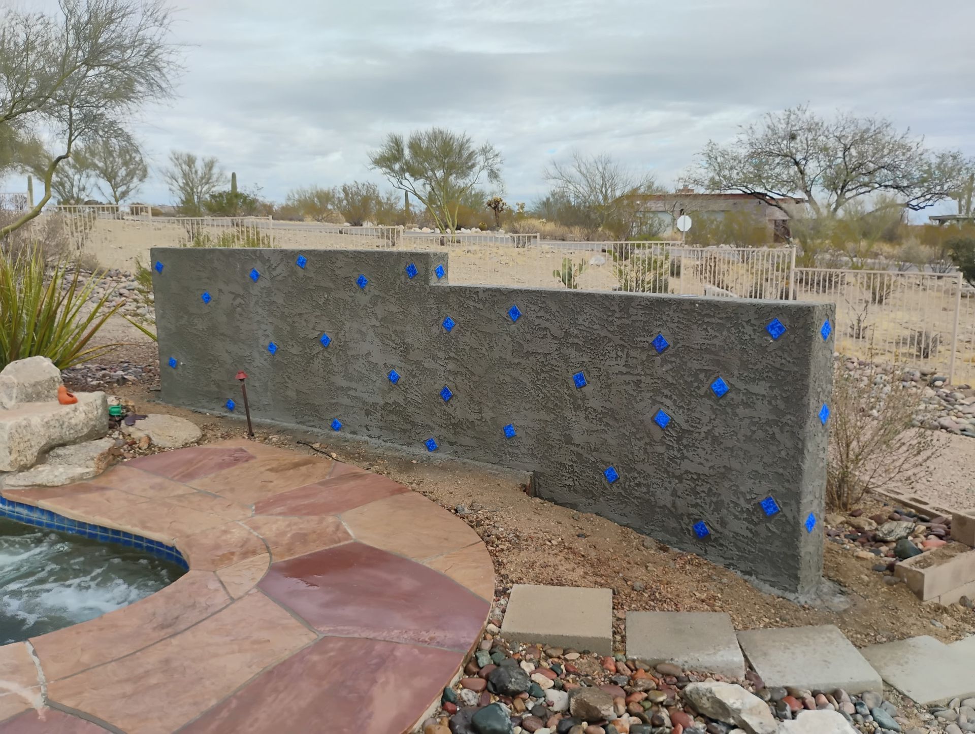 Concrete wall with blue tape dots, next to a pool and desert landscape.