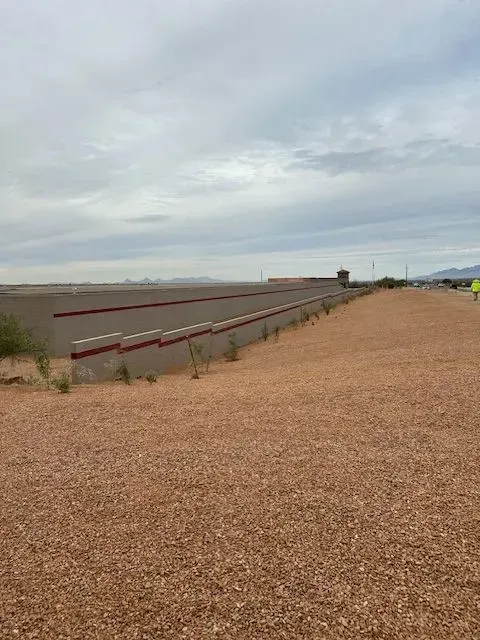 Gray sky over a gravel area with a low concrete wall featuring red stripes and sparse vegetation.