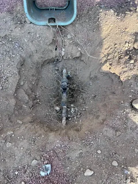 Underground irrigation system components in a dug-out area with wires and an above-ground plastic box.