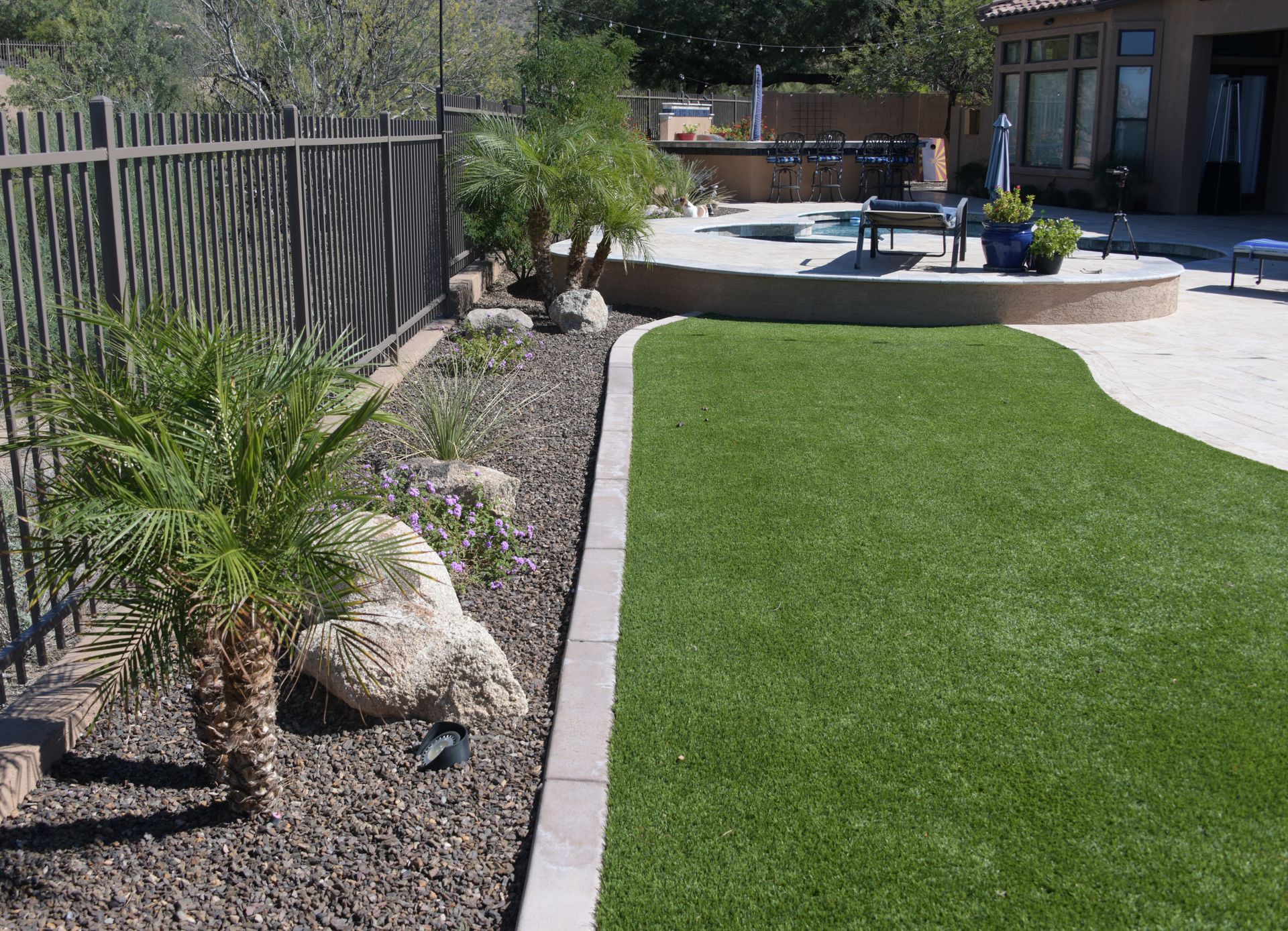 A backyard with artificial turf, landscaping, a fence, and a pool in the background.