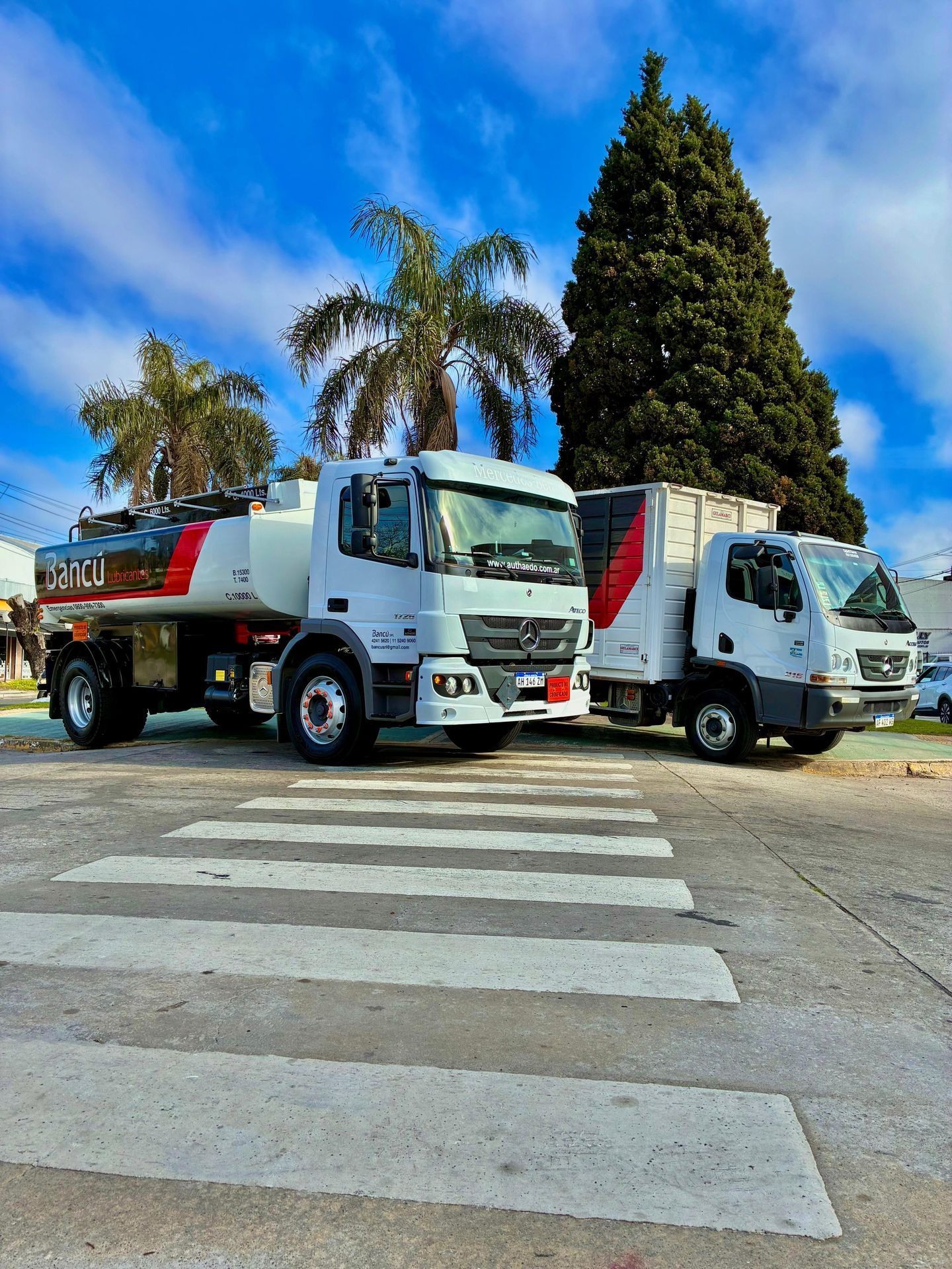 Dos camiones blancos estacionados en un cruce de peatones, uno de ellos es un camión cisterna de combustible