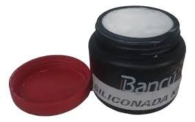 Tarro negro de crema de silicona blanca, con tapa roja al lado.