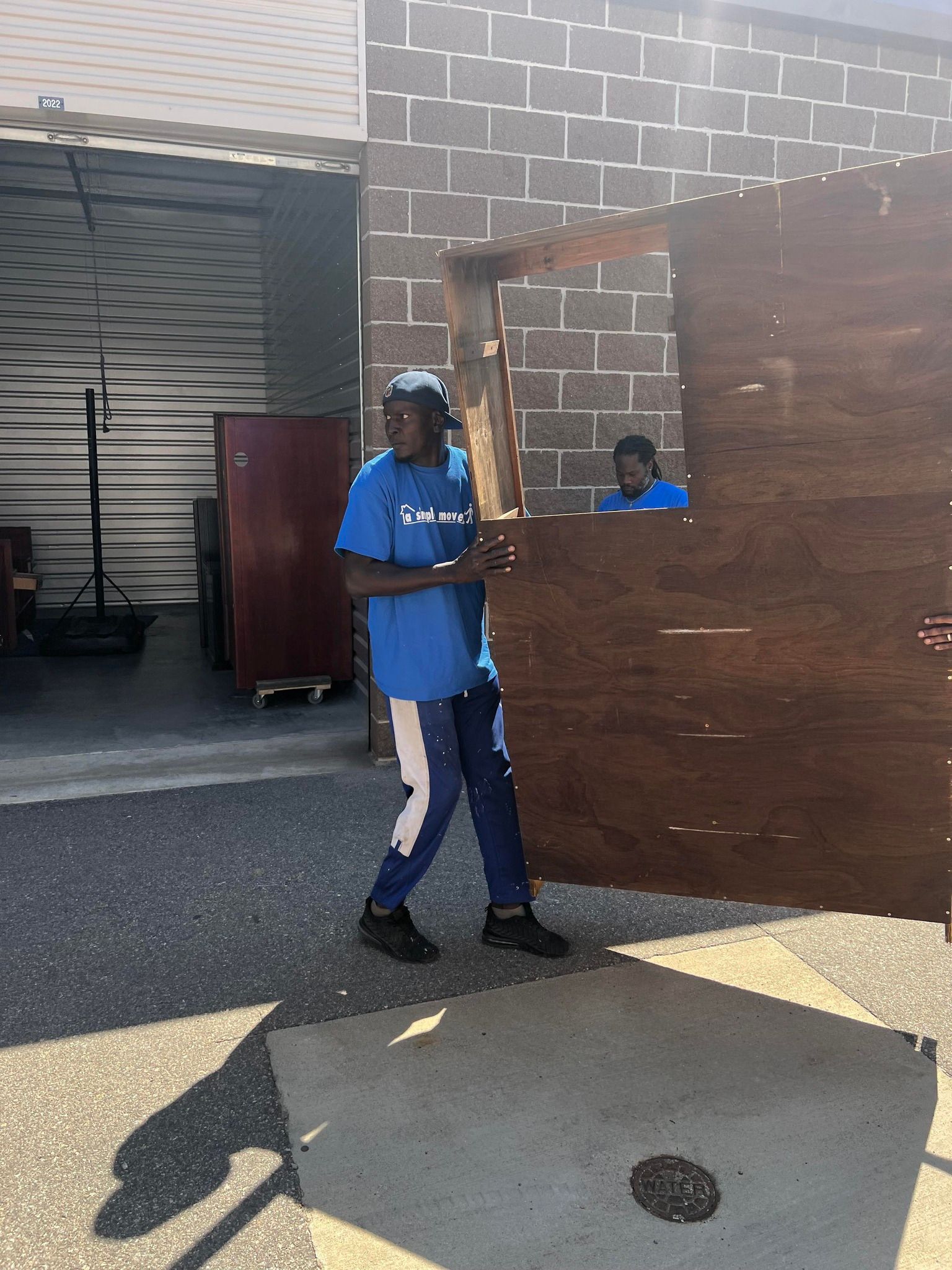 A man in a blue shirt is carrying a large piece of wood.