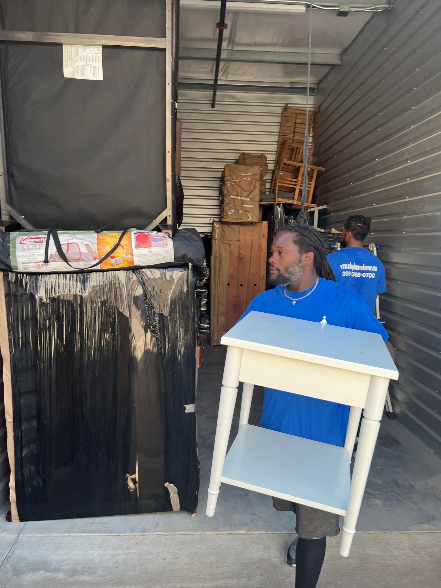 A man in a blue shirt is carrying a white table.