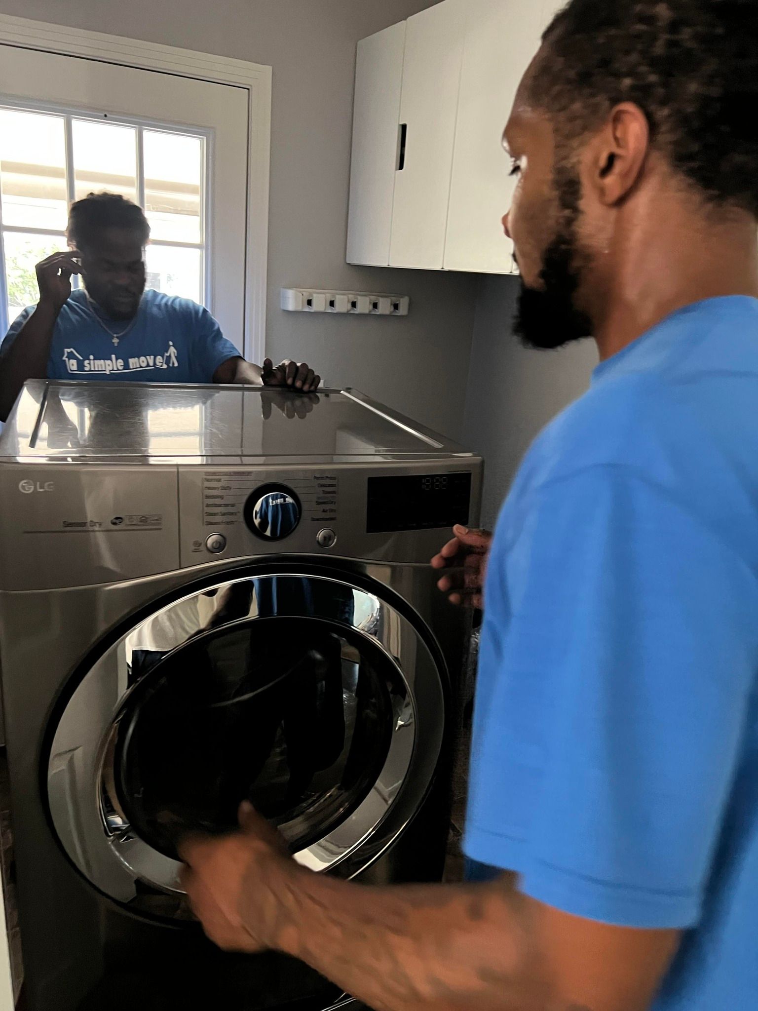 A man in a blue shirt is standing in front of a washing machine.