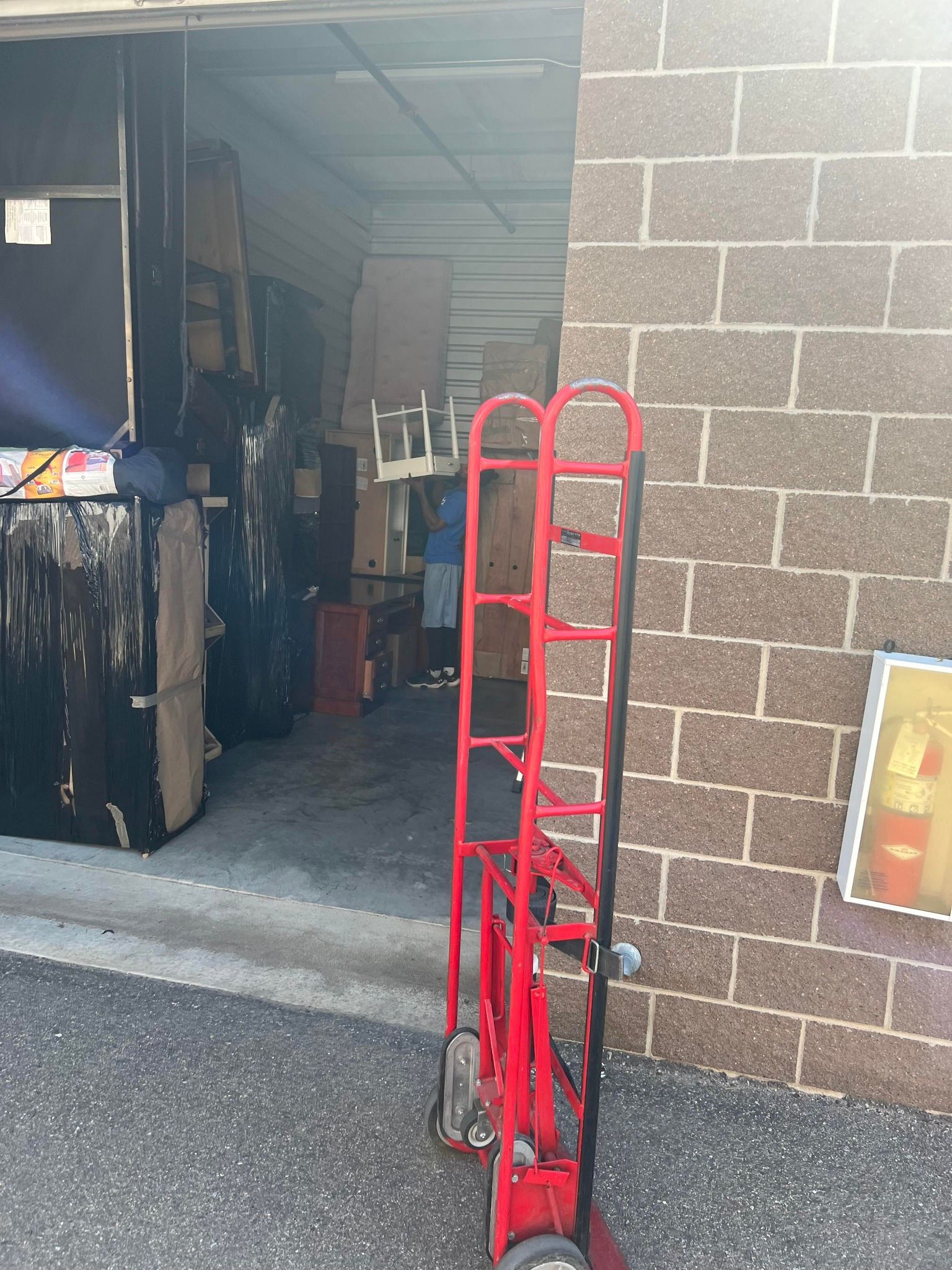 A red hand truck is parked in front of a brick building.