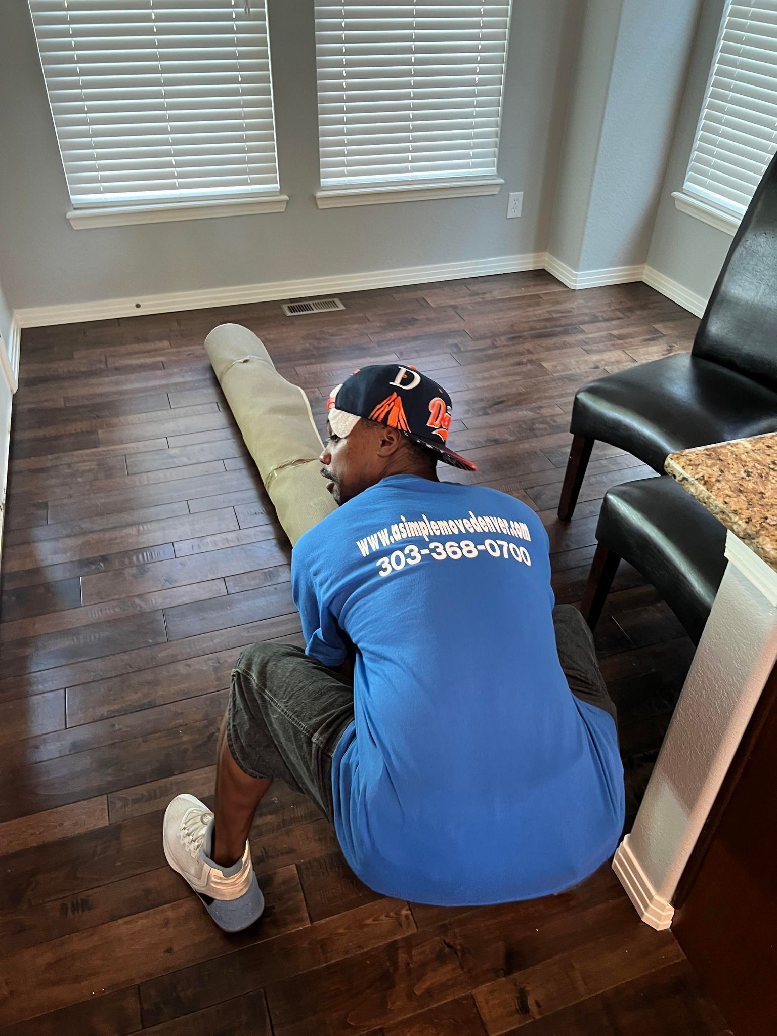 A man in a blue shirt is sitting on the floor in a living room.