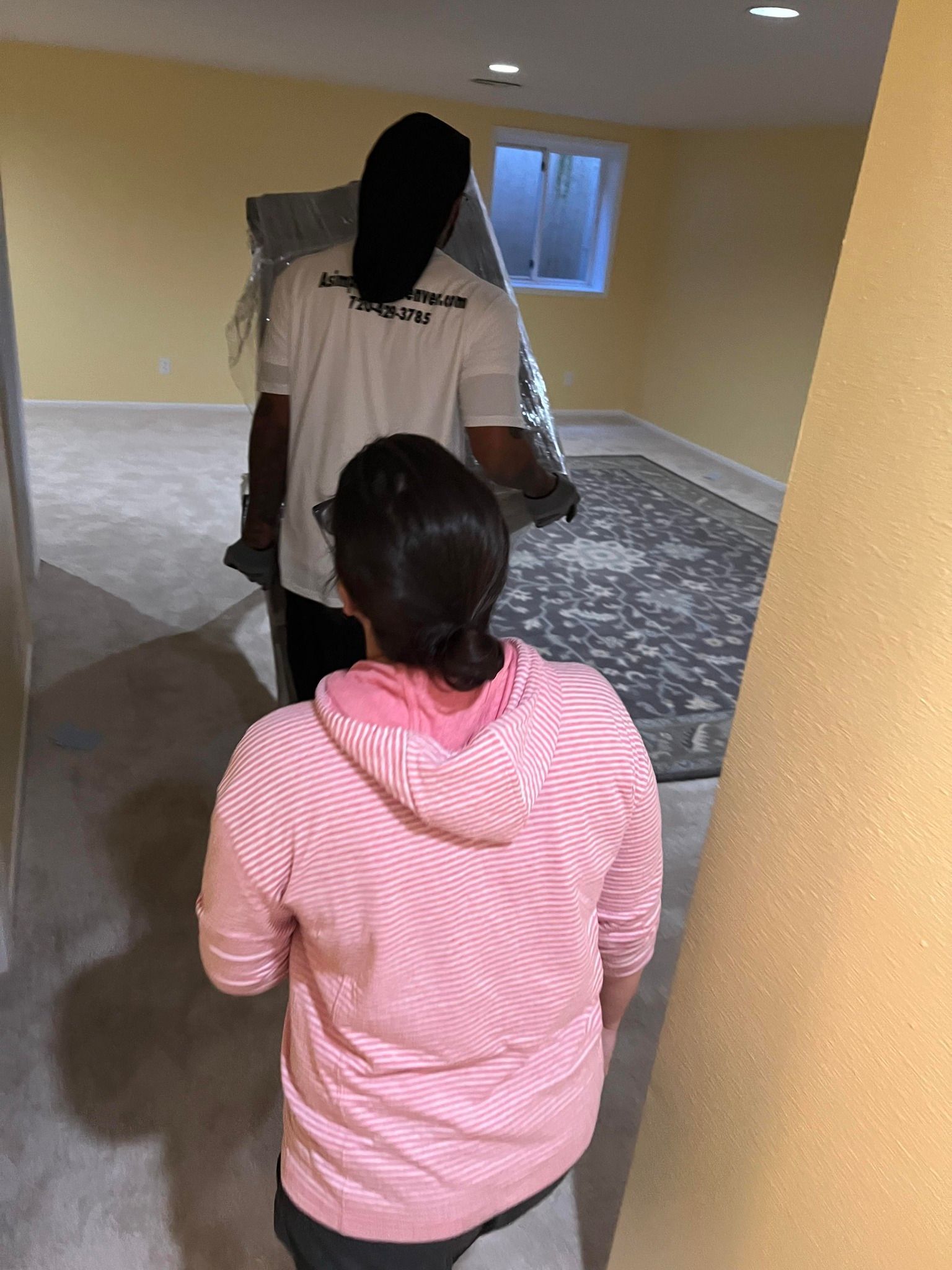 A man and a woman are carrying a mattress in a room.
