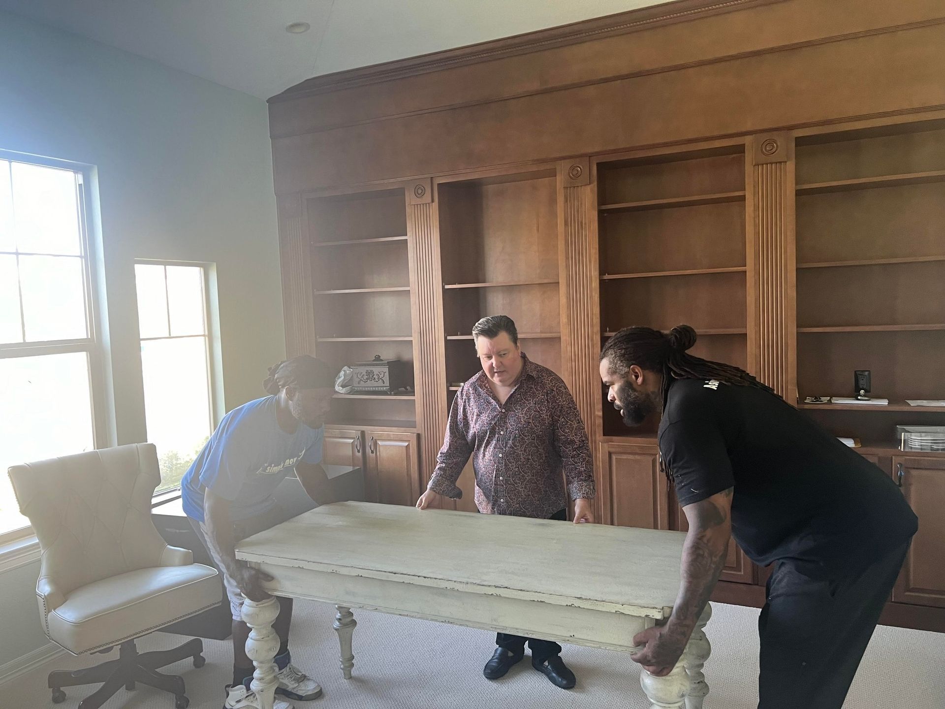 Three men are moving a table in a living room.