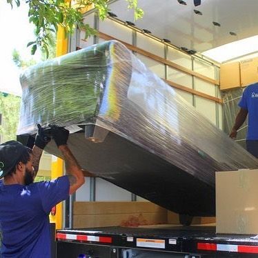 A man in a blue shirt is loading a large piece of furniture into a truck