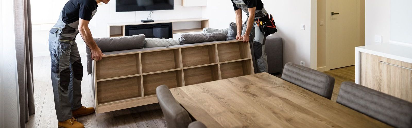 Two men are moving a wooden shelf into a living room.