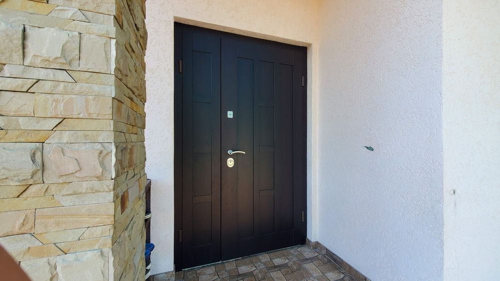 Una porta nera è appoggiata su un muro bianco, accanto a un muro di pietra.