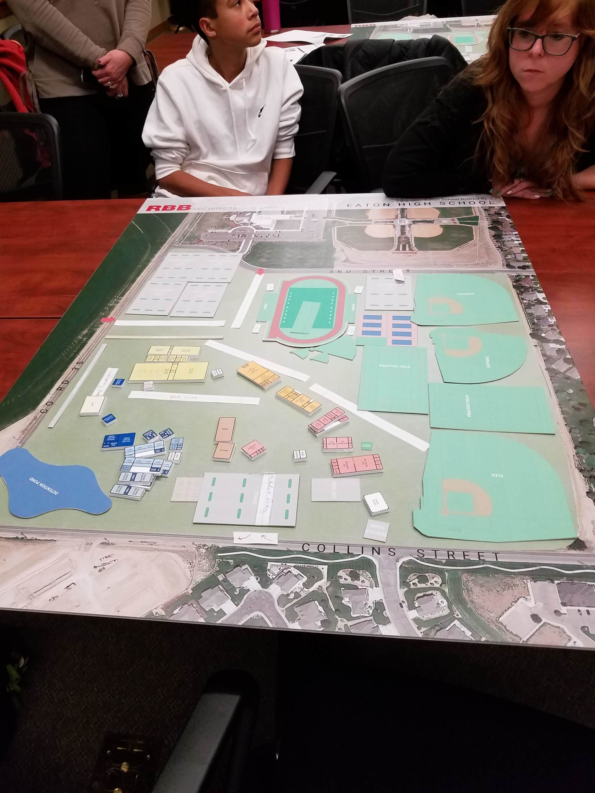 A group of people are sitting around a table with a model of a park on it