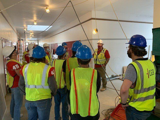 A group of construction workers wearing yellow vests and hard hats are standing in a hallway.