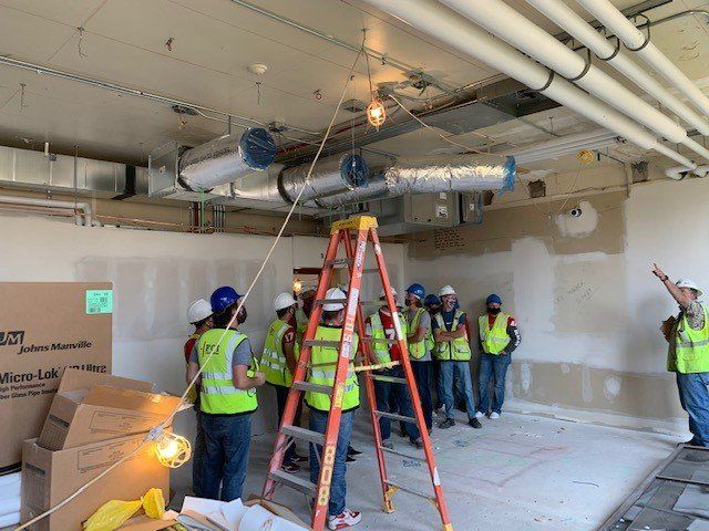 A group of construction workers are standing around a ladder in a room.