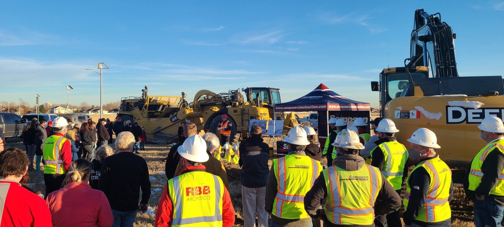 A group of construction workers are standing in front of a large excavator.