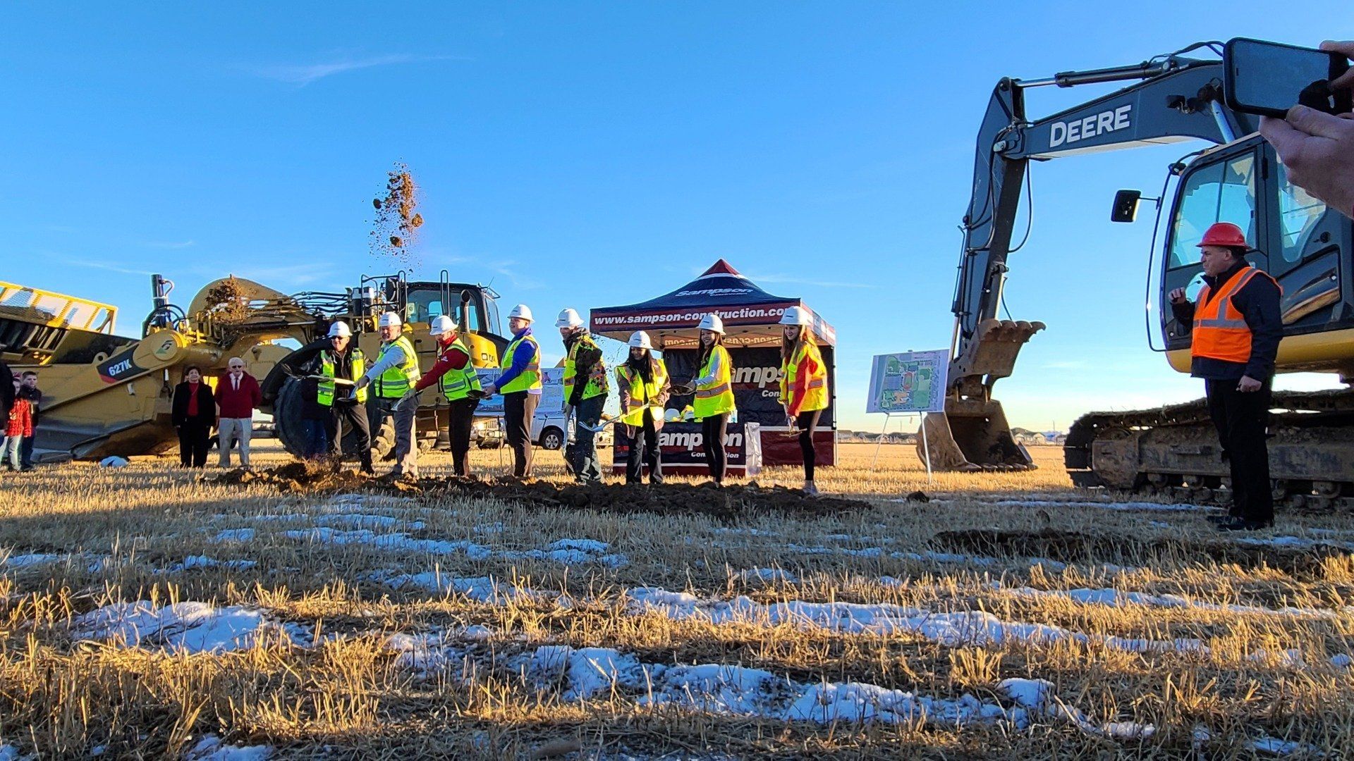 A group of construction workers are standing in a field next to a large excavator.
