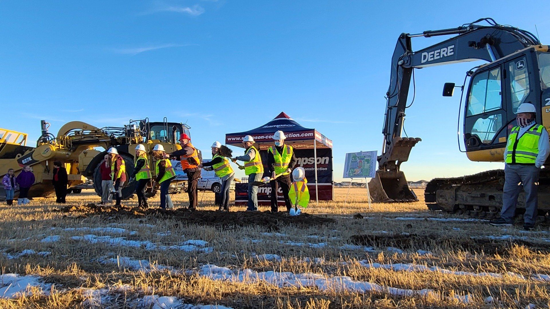 A group of construction workers are standing in a field next to a large excavator.