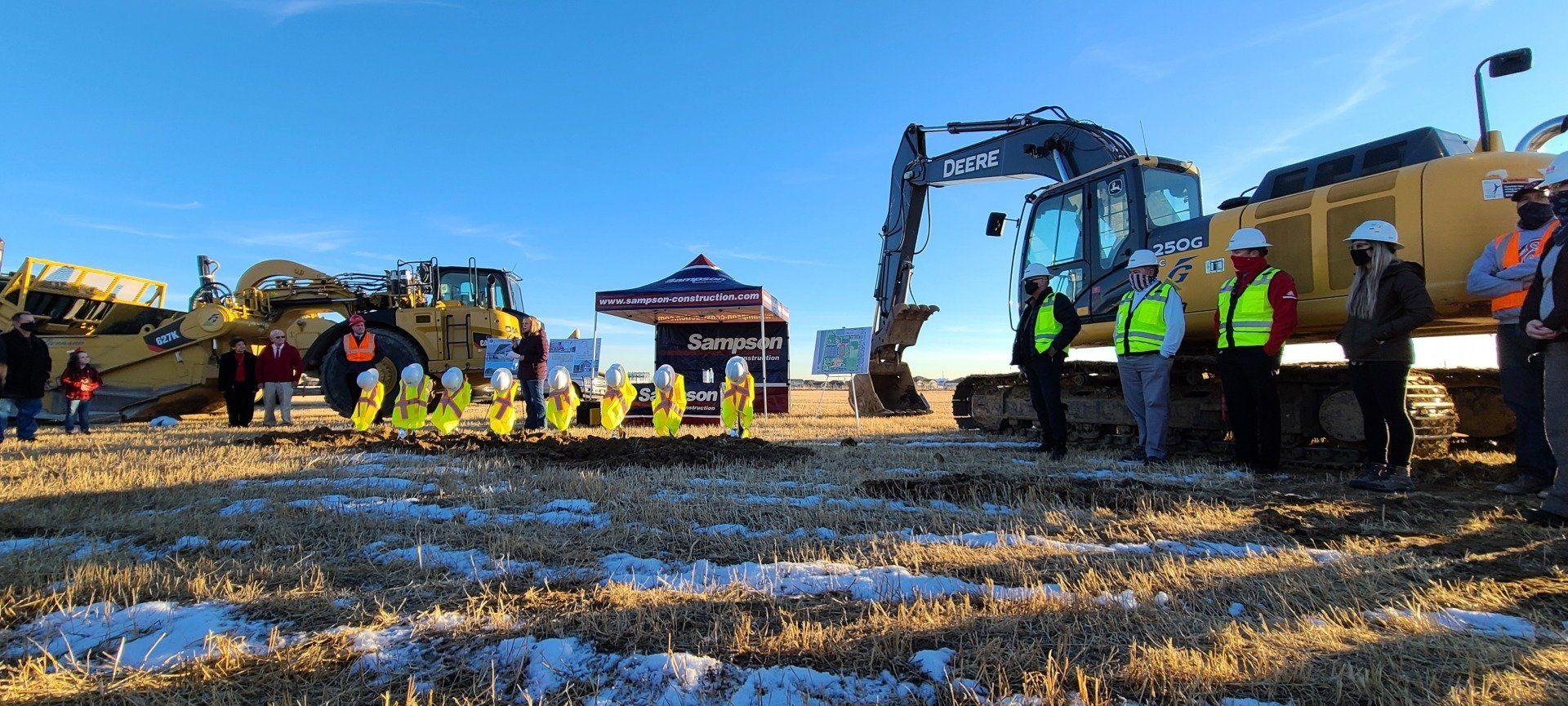 A group of construction workers are standing in a field with tractors.