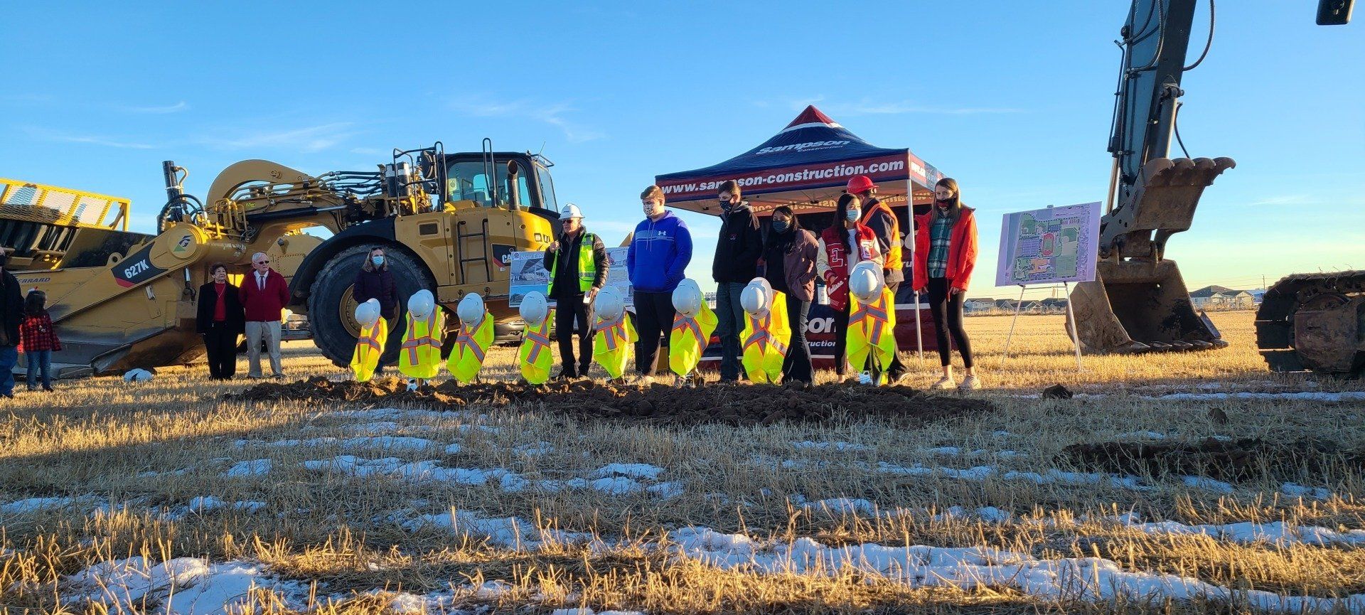 A group of people are standing in a field next to a bulldozer.
