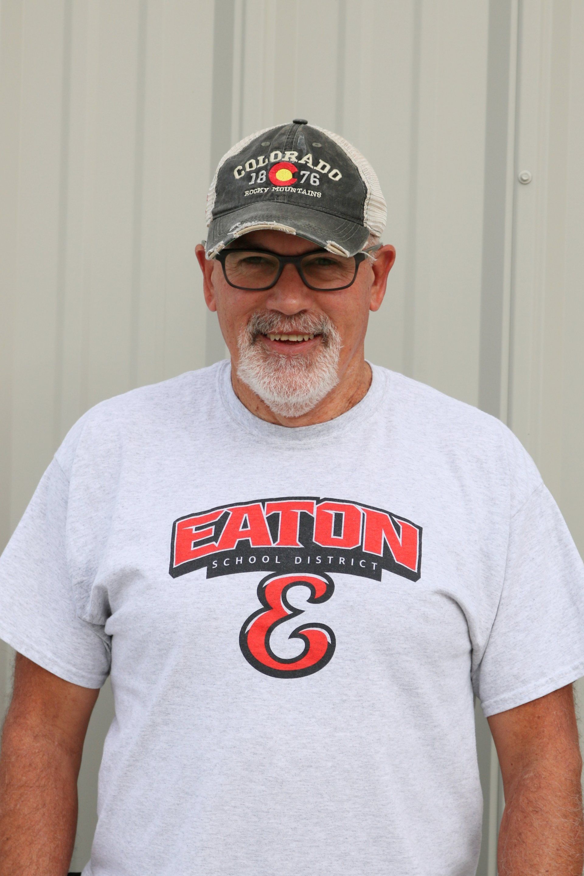 A man wearing a hat and glasses is wearing a eaton shirt.