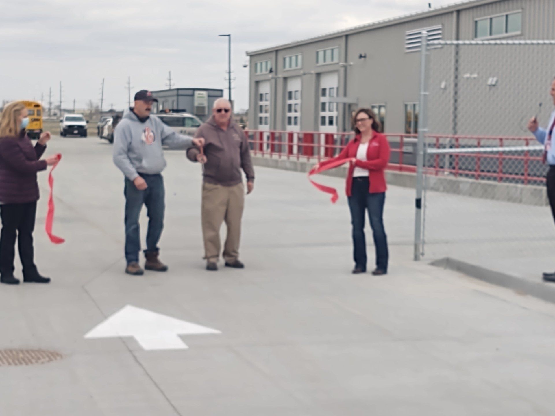 A group of people cutting a red ribbon in front of a building
