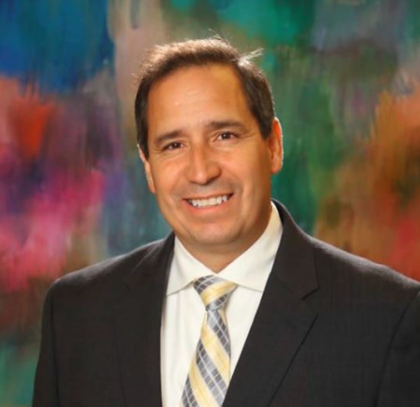 A man in a suit and tie is smiling in front of a painting