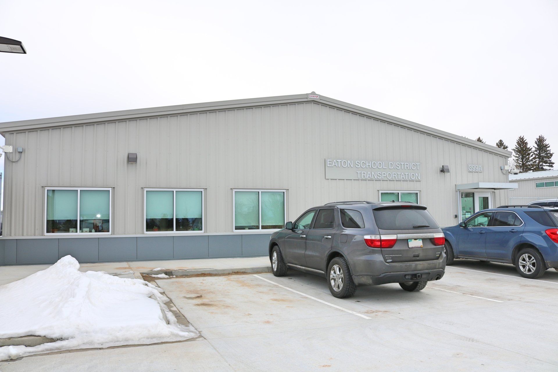 Two cars are parked in front of a building with snow on the ground.