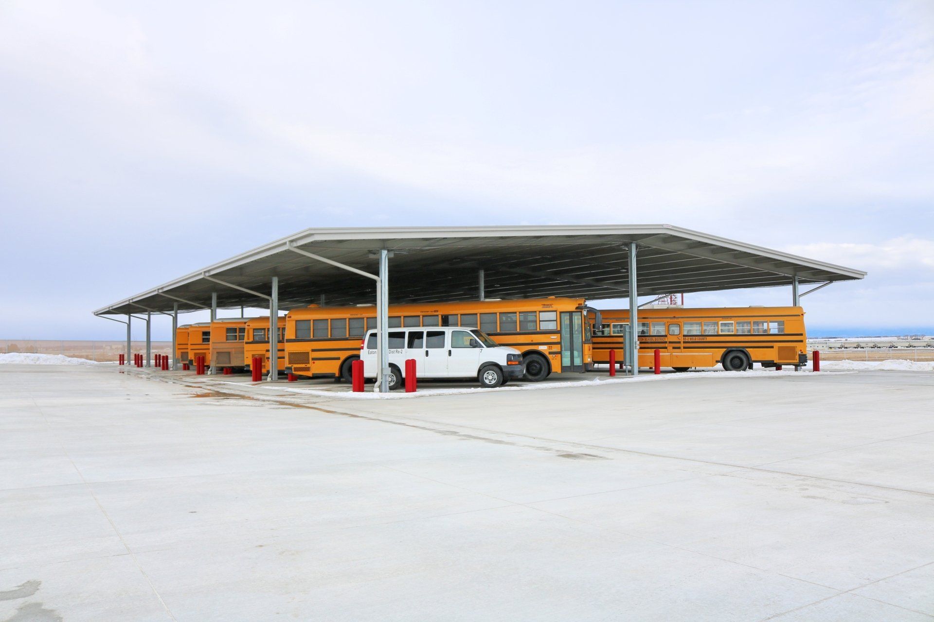 A row of school buses are parked under a covered area