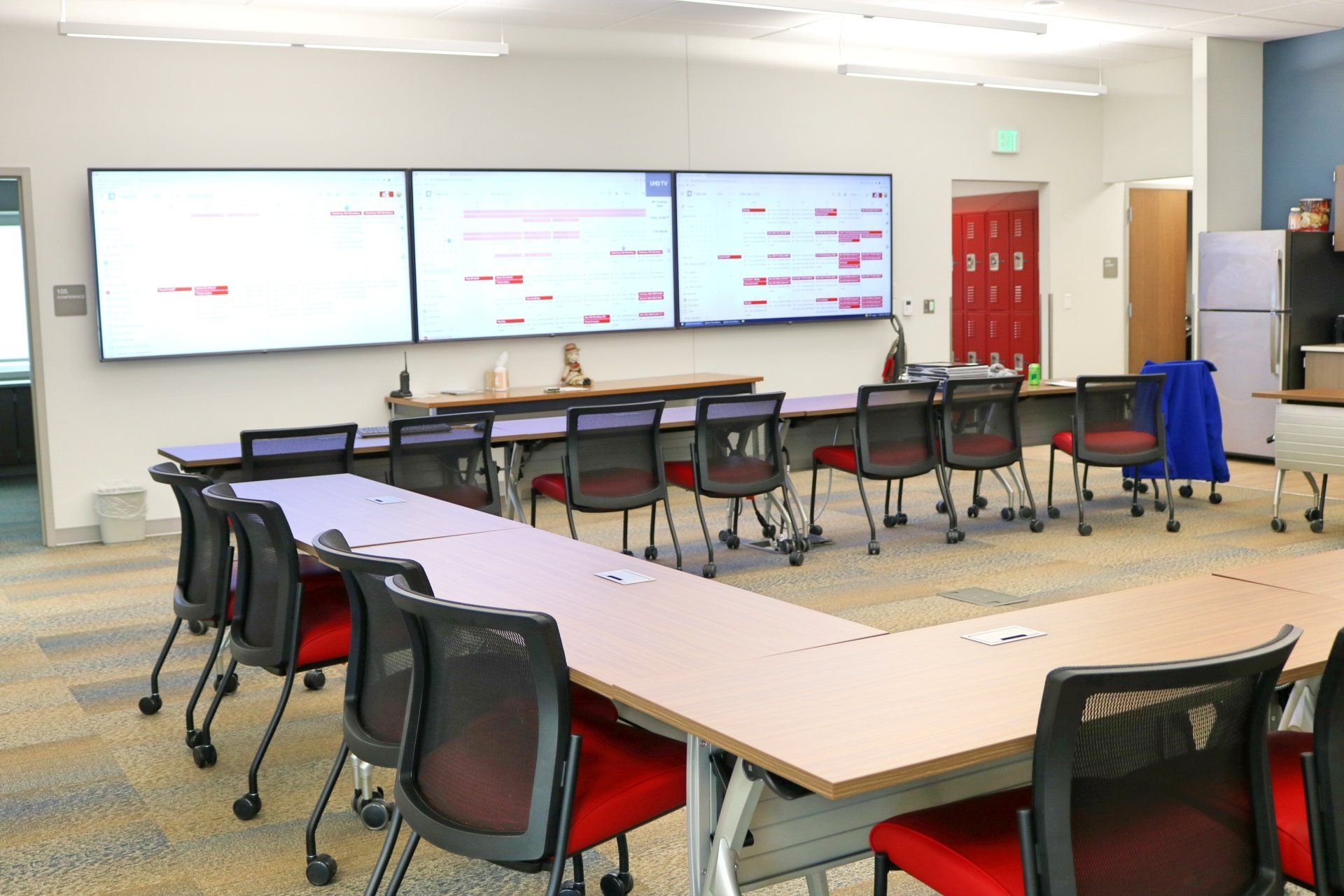 A classroom with tables and chairs and a large screen on the wall.