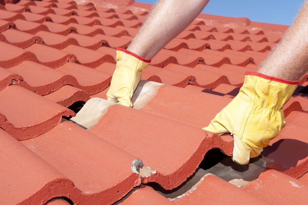 Worker With Yellow Gloves Replacing Red Tiles Or Shingles On House — Munro Building Group In Logan, QLD