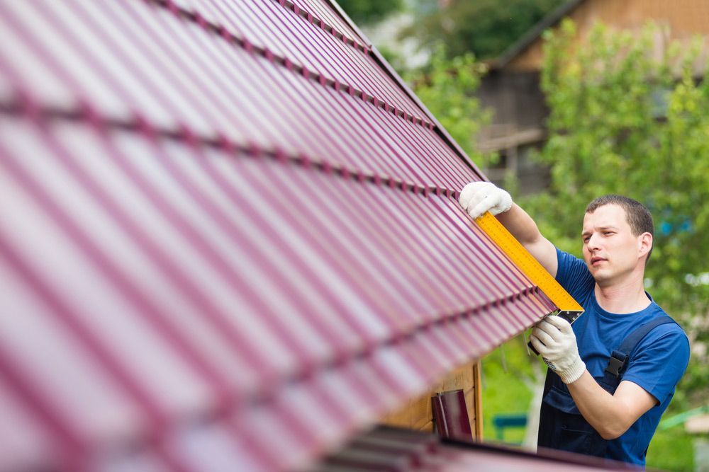 A Man In A Blue Shirt Is Working On A Roof — Munro Building Group In Logan, QLD
