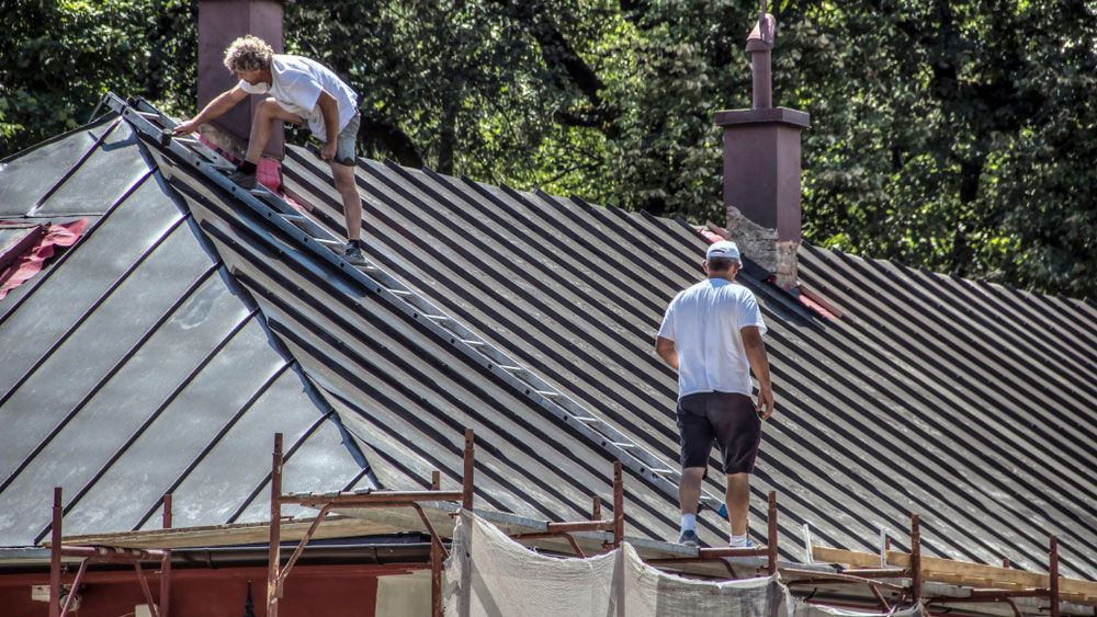 roofers in Logan inspecting a large metal roof for damage during a residential repair project