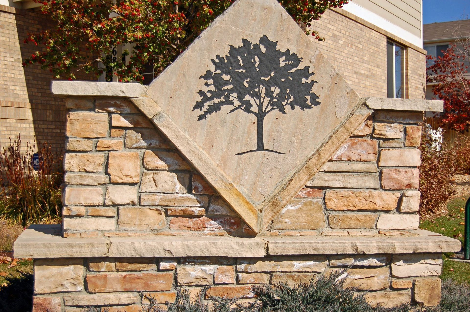 Stone monument sign with a tree emblem set in a landscaped outdoor setting