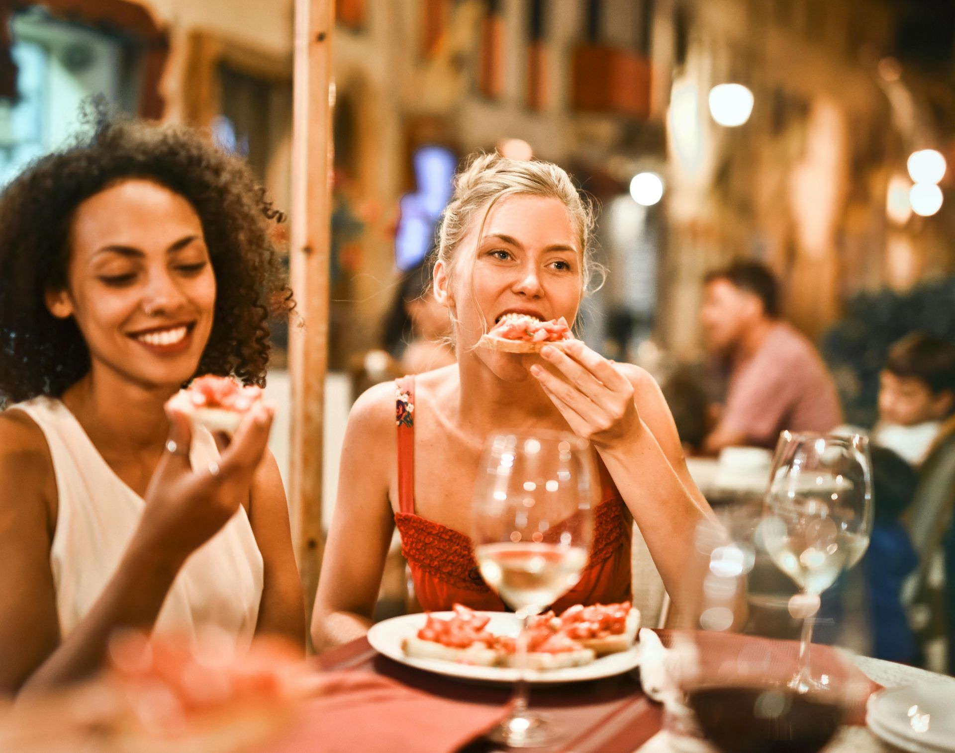 Two friends smiling and eating dessert at a warmly lit restaurant table