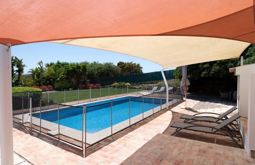 Fenced Swimming Pool In Garden With Sunbeds Under A Shade Sail — Shade Sails in Lismore, NSW