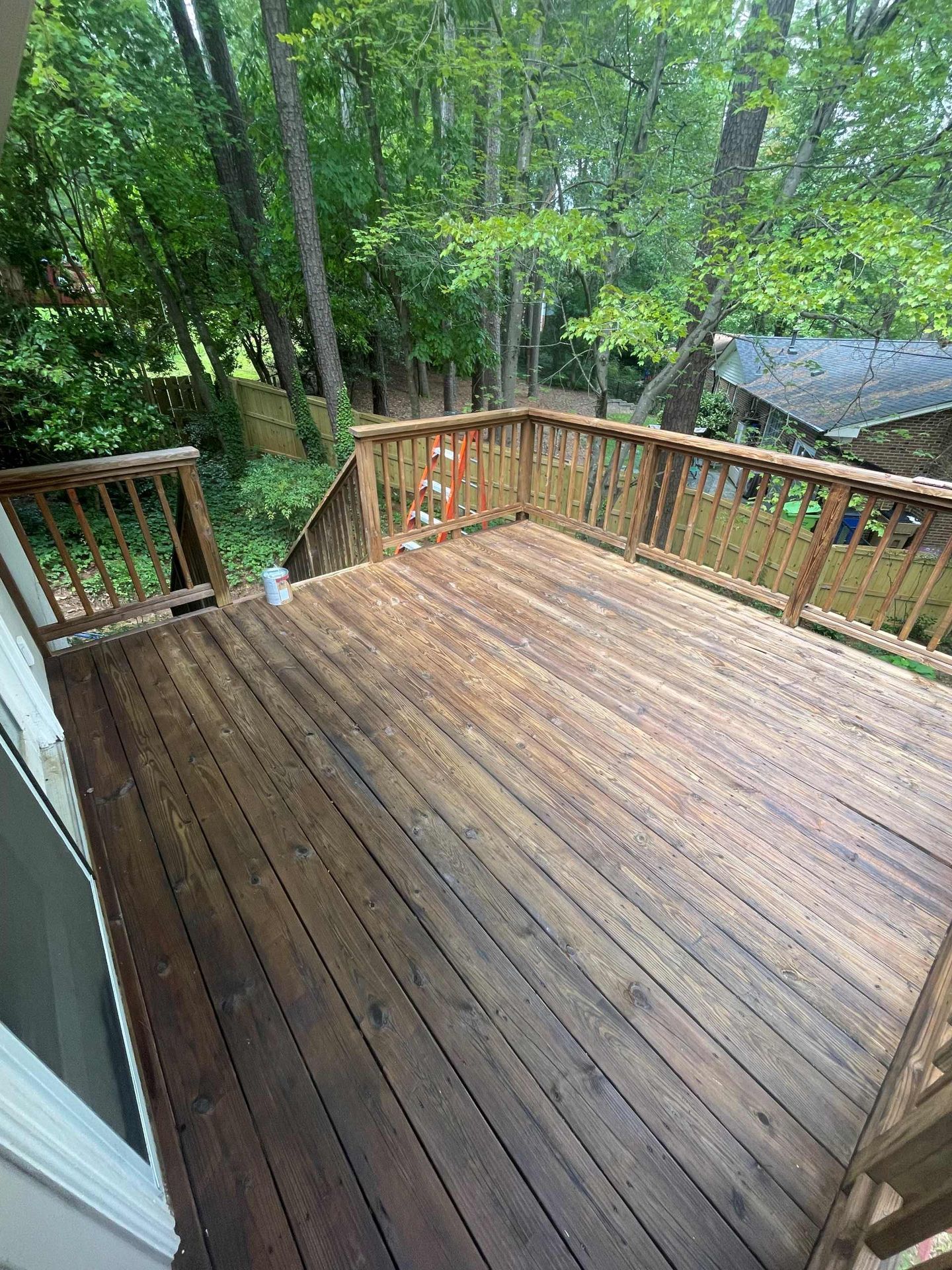 Wooden deck with railings, surrounded by trees and a house roof.
