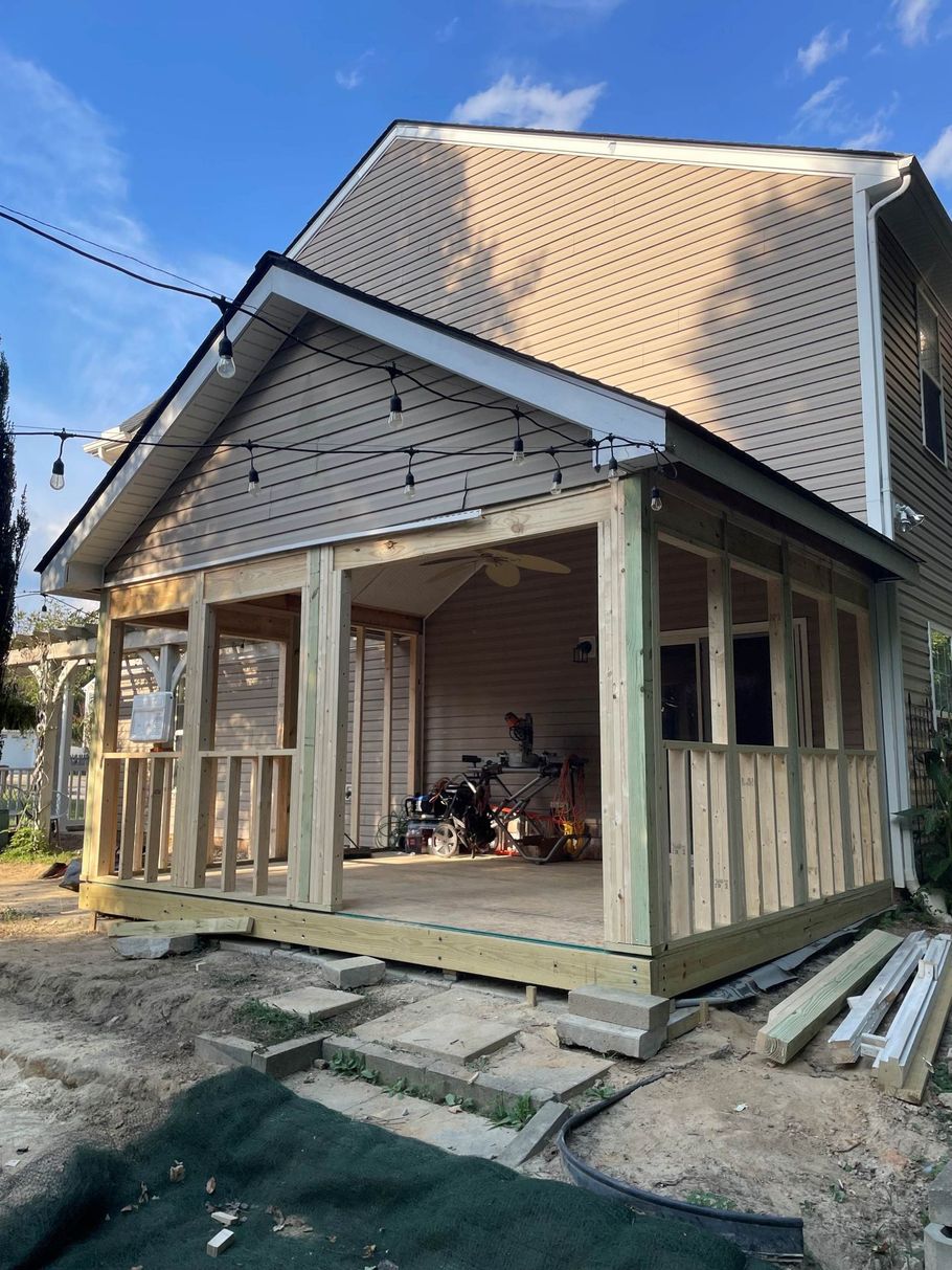 New wooden porch addition attached to a two-story beige house under construction.