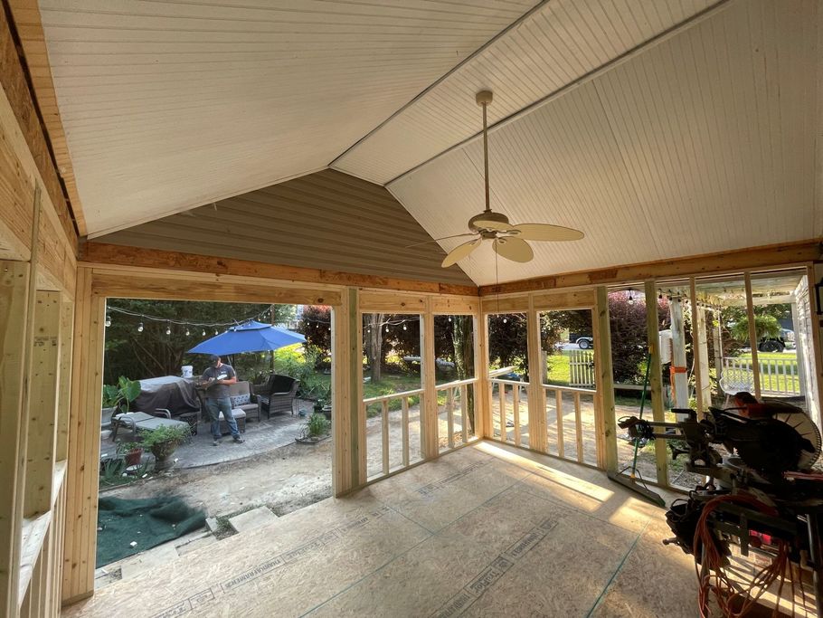 Interior view of a sunroom under construction, open to a backyard patio with a pool and umbrella.