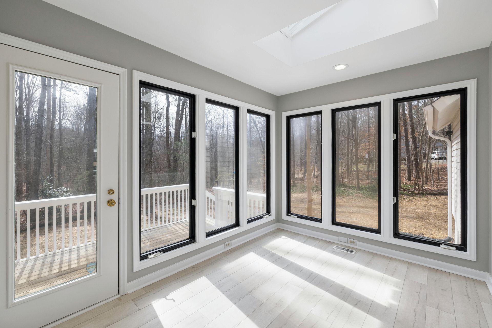 Sunroom with large windows, door to a deck, and skylight, with a view of trees.