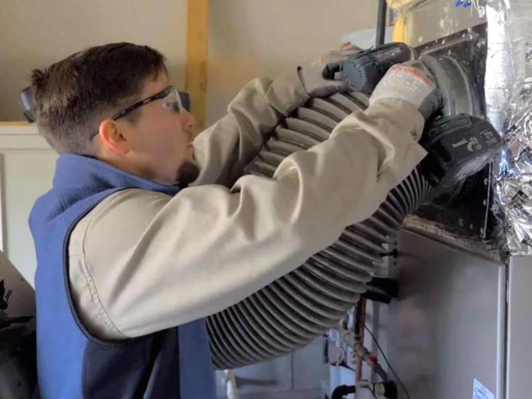 HVAC technician in safety glasses connects flexible ductwork to an air handler unit.